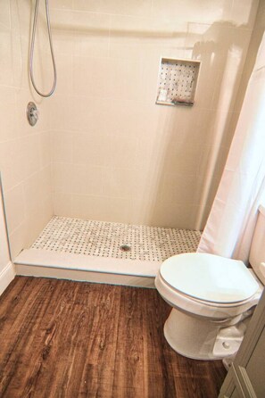 A bathroom with a shower, a toilet, and a wooden floor.