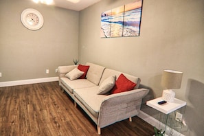 A living room with a sofa, a clock, a painting, and a lamp.