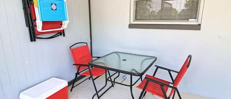 Un patio con una mesa de vidrio y dos sillas rojas, un refrigerador rojo y un armario azul contra una pared azul claro.