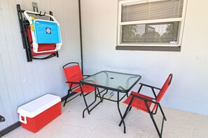 A patio with a glass table and two red chairs, a red cooler, and a blue storage unit against a light blue wall.