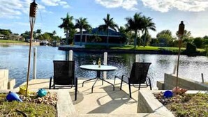 A waterfront patio with a table and chairs, overlooking a calm lake and a boat dock. - The Cape 3 Gulf access (Cape Coral)