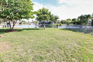 A grassy outdoor area with a fenced pool, trees, and a clear sky.