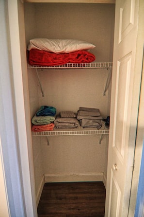 A walk-in closet with two shelves, one above the other, containing folded clothes and a red blanket.
