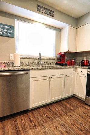 A kitchen with white cabinets, a granite countertop, a stainless steel dishwasher, and a red coffee maker.