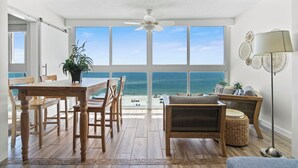 Amplia habitación con un gran ventanal con vistas al océano, una mesa de comedor de madera y una zona de estar acogedora con una lámpara de pie.