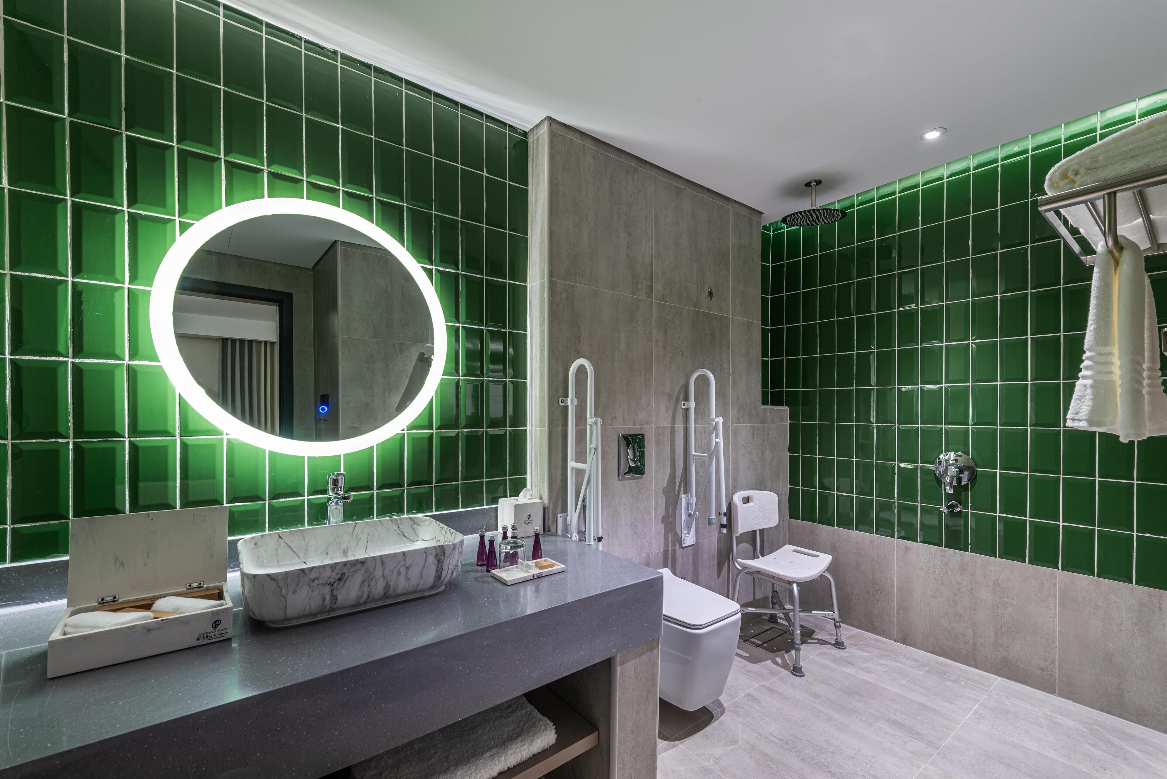 A modern bathroom with a marble sink, a large mirror, and green-tiled walls.
