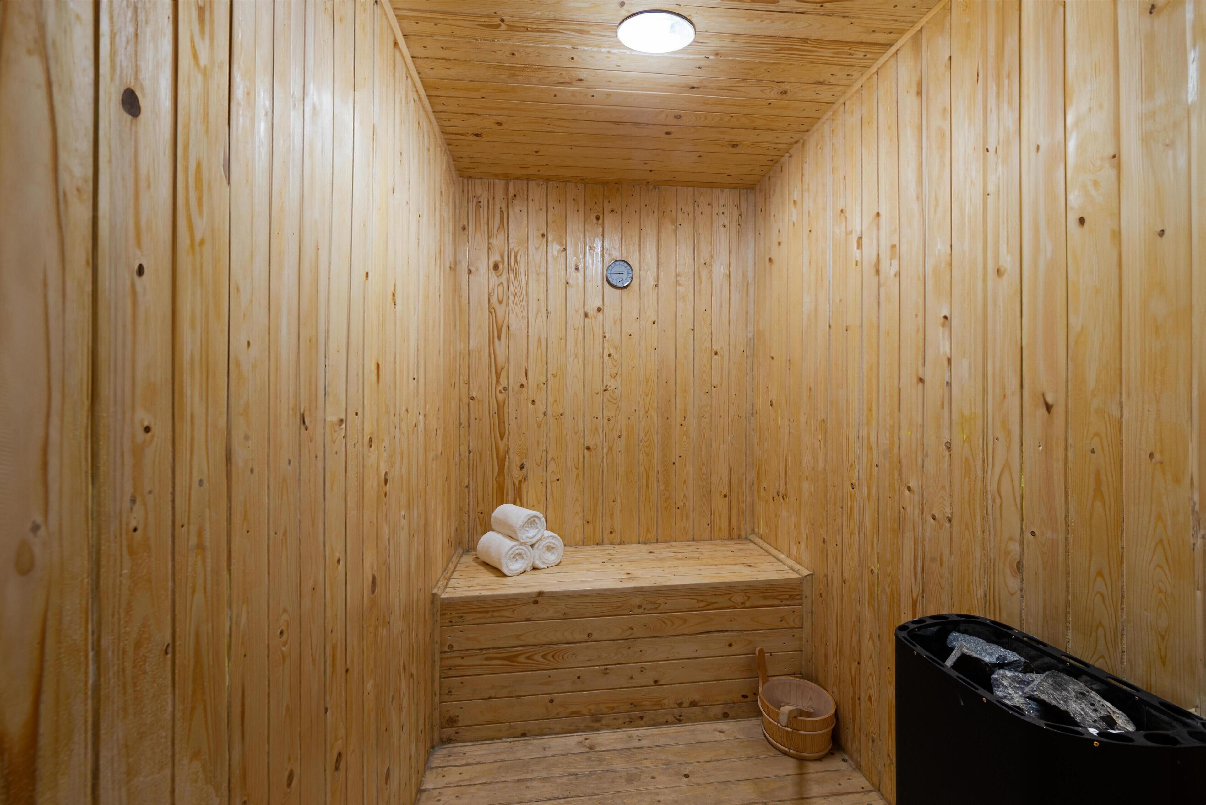 A wooden sauna with a bench, a clock, and a trash bin.
