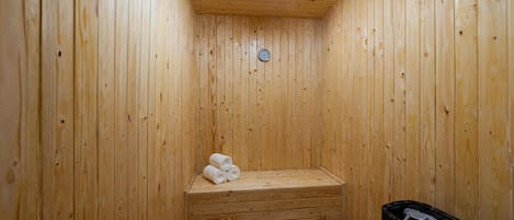A wooden sauna with a bench, a clock, and a trash bin.