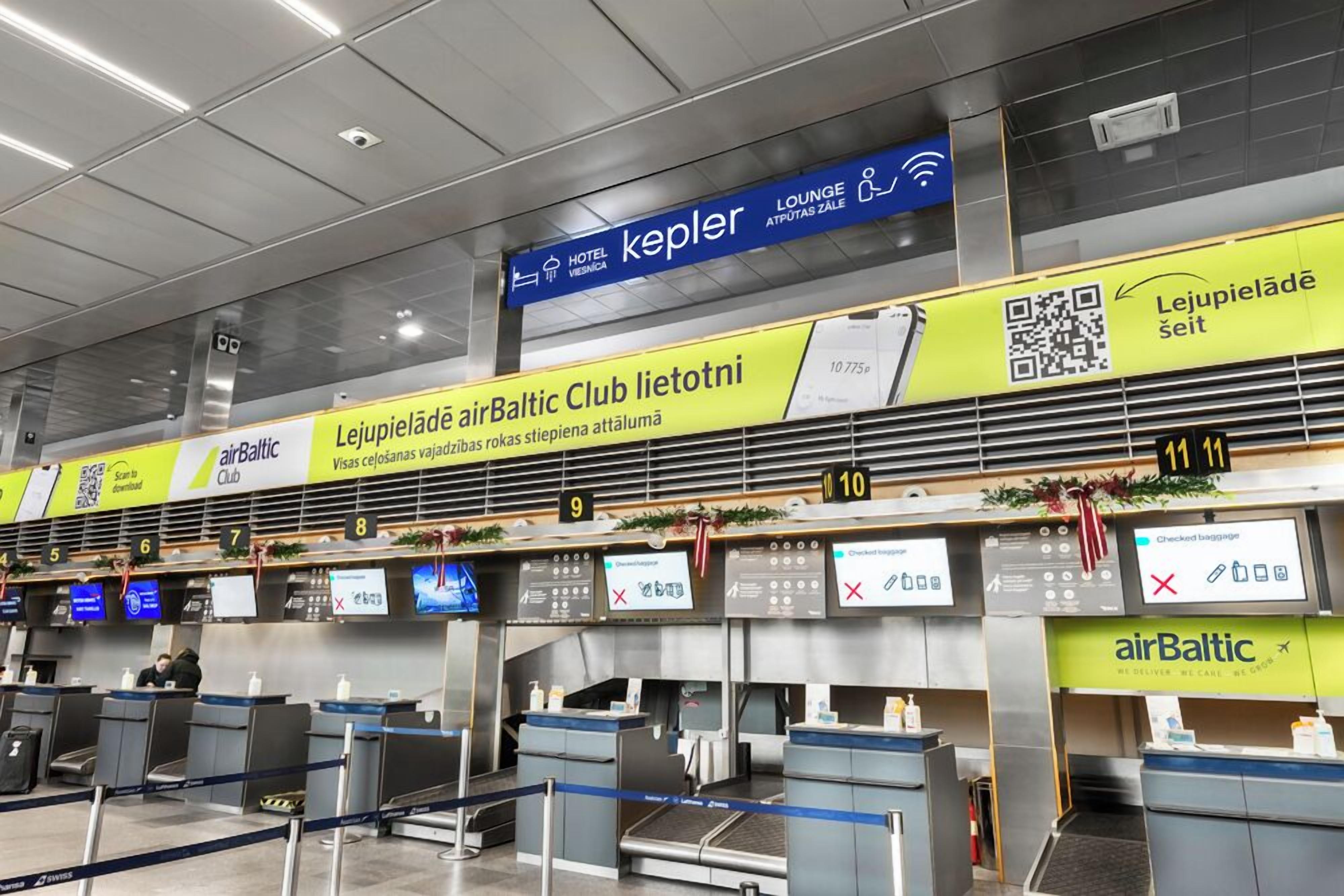 Lentokentän sisäänkirjautumisalue, jossa on useita palvelutiskiä sekä opasteet hotelleille: »airBaltic Club», »Lejupieladā» ja »Kepler».
