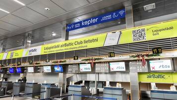 Lentokentän sisäänkirjautumisalue, jossa on useita palvelutiskiä sekä opasteet hotelleille: »airBaltic Club», »Lejupieladā» ja »Kepler».