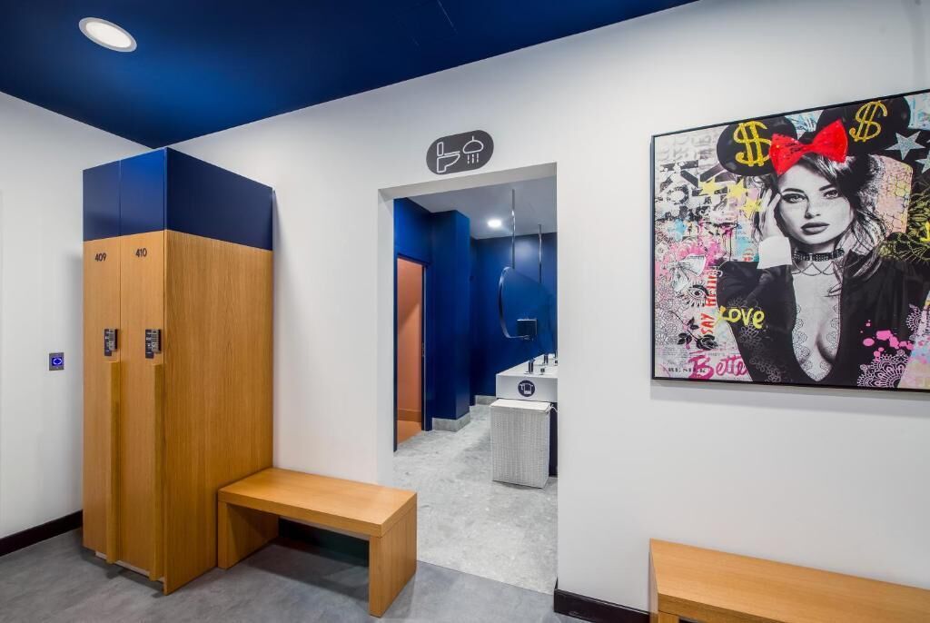 Un pasillo con taquillas, un banco, un baño y una pared con un cartel colorido.