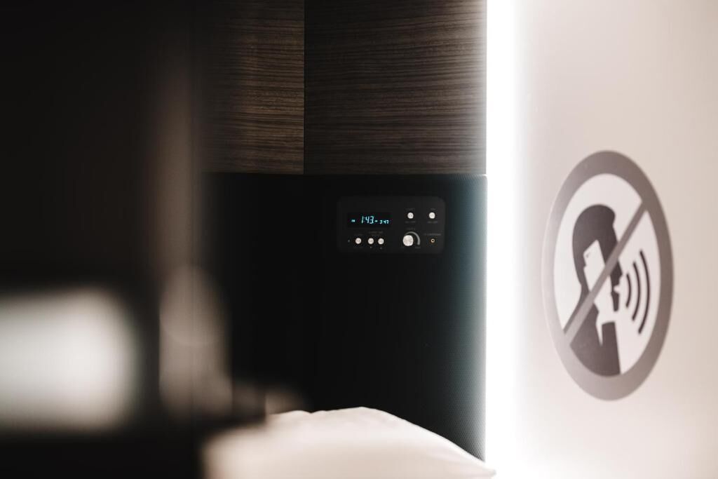 Un panel de control con pantalla digital y botones, y un cartel de prohibición de teléfonos móviles en la pared.
