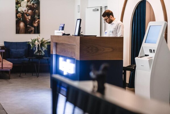A reception desk with a digital kiosk, a blue sofa, and a vase with flowers.