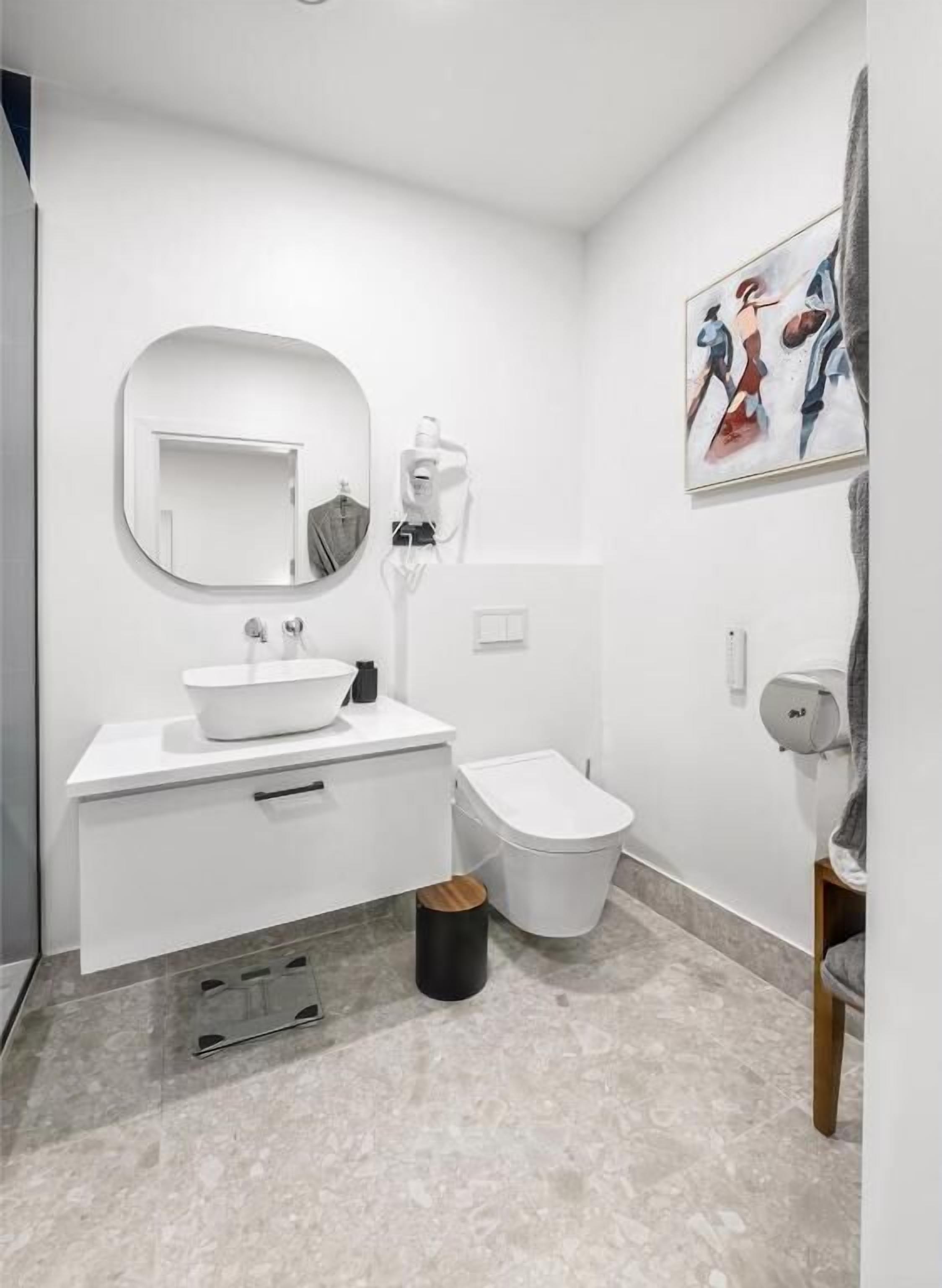 A modern bathroom with a white sink, mirror, and toilet.