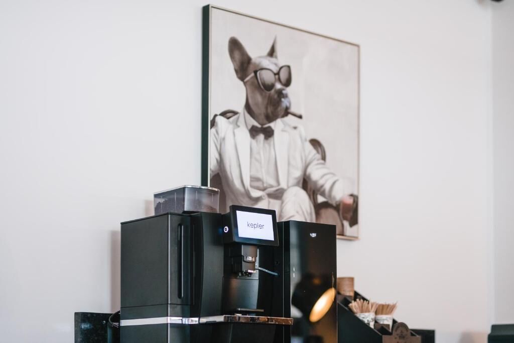 A coffee machine with a label that reads "kepler" and a framed picture of a dog in a suit on the wall.