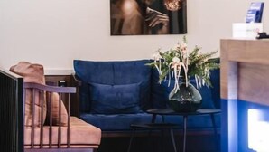 Un área de recepción moderna con un sofá azul, una mesita con un jarrón de flores y una obra de arte enmarcada en la pared.