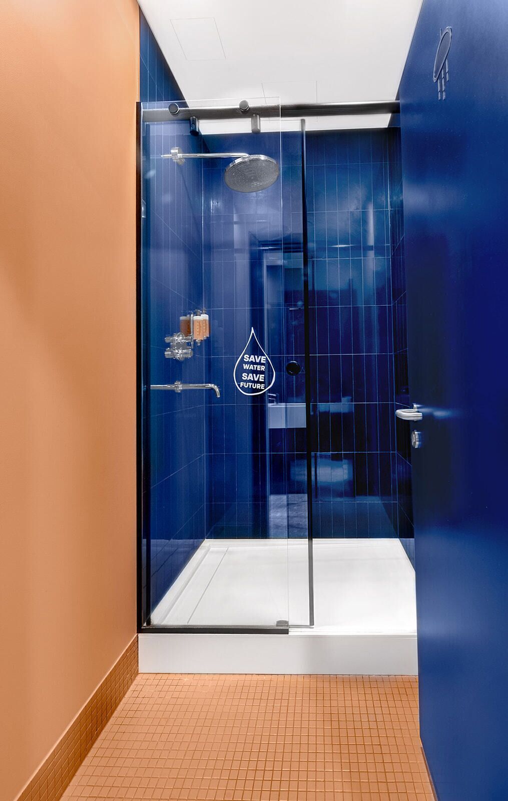 A modern bathroom with a glass-enclosed shower, blue tiles, and a 'SAVE WATER SAVE FUTURE' sign.