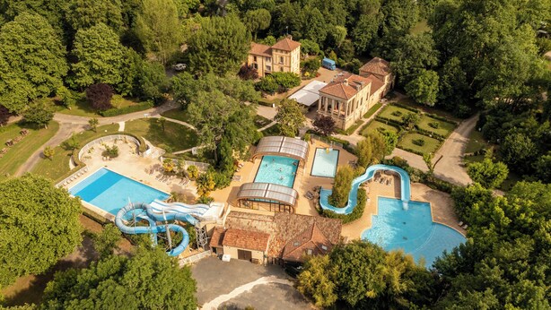 An aerial view of a resort with multiple swimming pools, a water slide, and a large building.