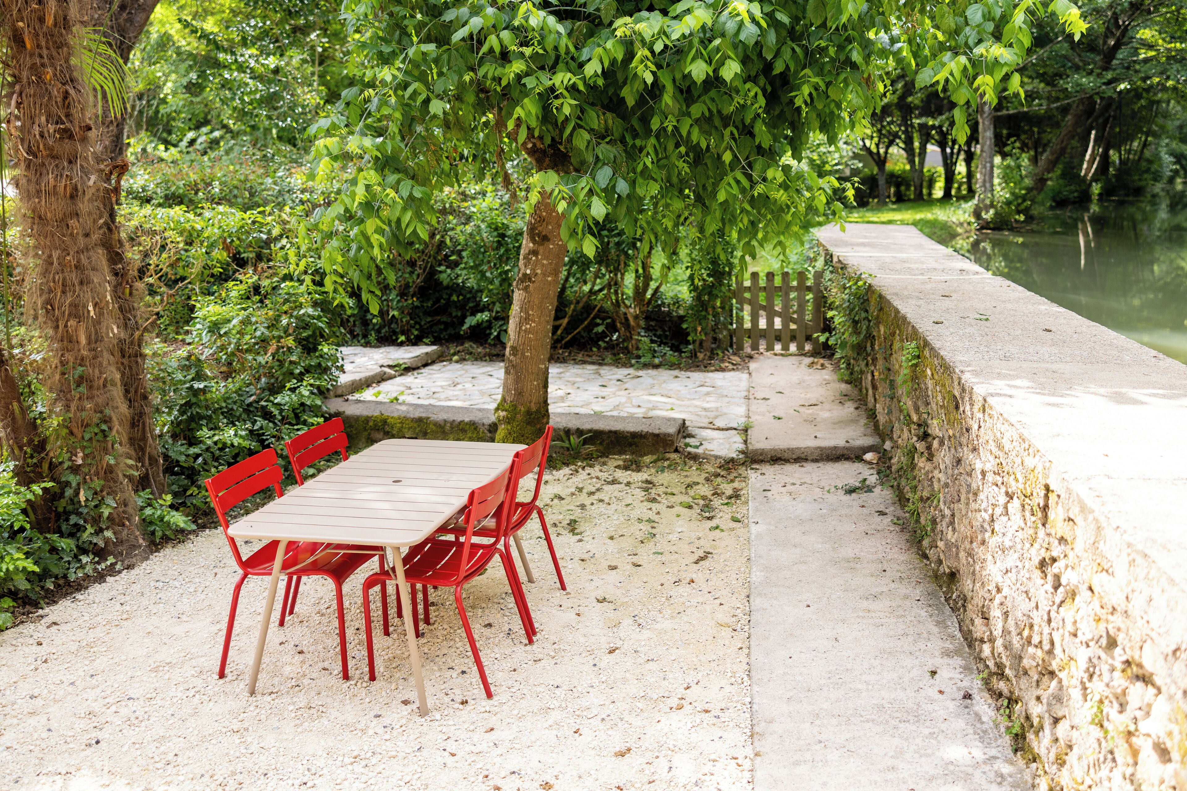 Een betonnen tafel en stoelen staan buiten, met een stenen muur en een houten omheining in de buurt.