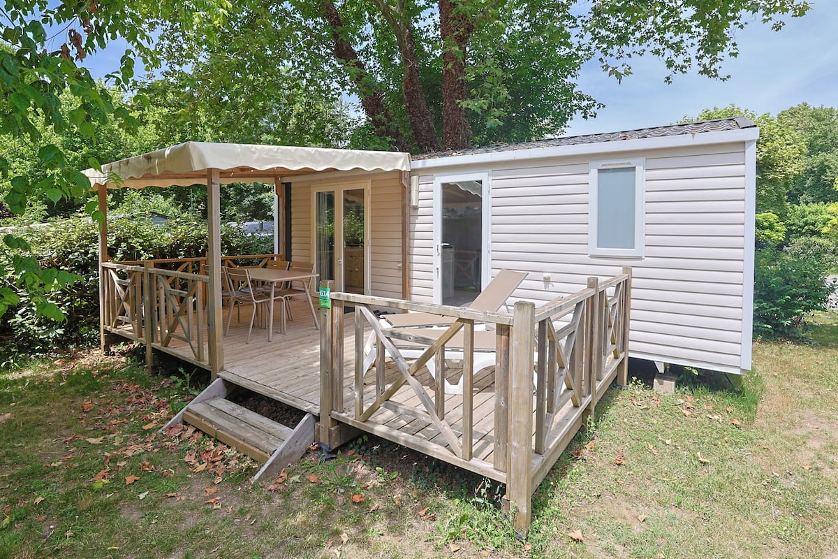A mobile home with a covered patio, outdoor seating, and a small window.