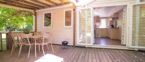 A wooden deck with a table and chairs, a covered patio area, and a view into a kitchen and living space.