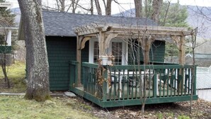 A small wooden structure with a green porch and a covered area, surrounded by trees and a grassy yard. - Quaint Private Bungalow (Woodstock)
