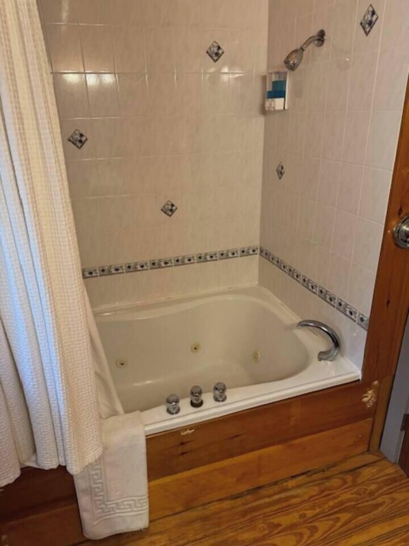 Un baño con bañera, ducha y suelo de madera.