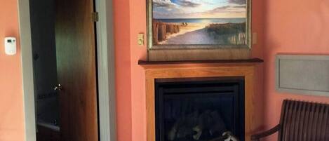 Une pièce avec une cheminée, un tableau au-dessus, et un lit avec un cadre en métal.