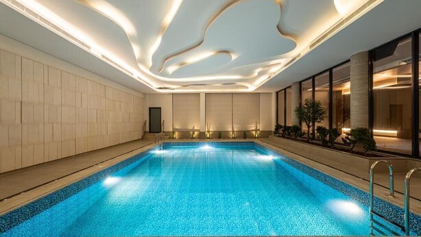 Une piscine au design moderne, entourée d’un sol carrelé et d’un mur de couleur claire.