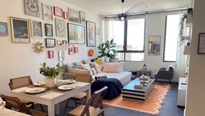 A modern living room with a dining area, a sofa, a coffee table, and a large window. - City view of Melbourne GPO | Sunlit 2BR residence (Melbourne)