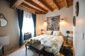 Un dormitorio con cama, escritorio, silla, espejo y ventana con cortinas.