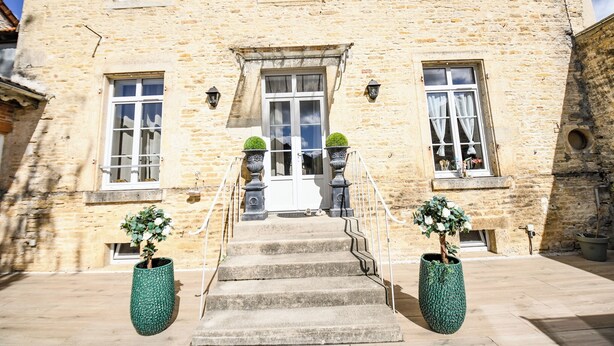 A stone building with a central entrance, two potted plants, and a staircase leading to the entrance.