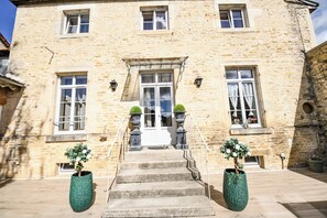 A stone building with a central entrance, two potted plants, and a staircase leading to the entrance.