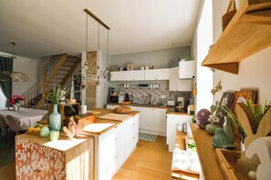 Een moderne keuken met witte kasten, een houten keukeneiland en een trap naar een zolderruimte.