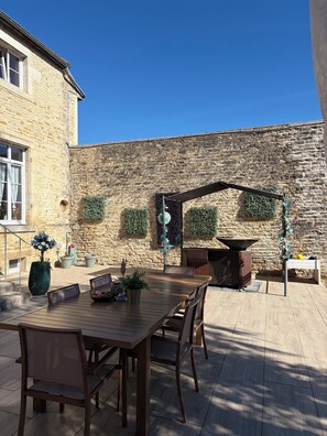 A patio with a stone wall, a wooden table, and chairs.