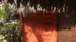 A red brick building with a thatched roof, a wooden door, and a woven screen.