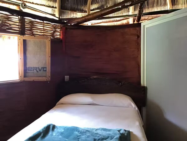 A small, single-bed room with a wooden headboard and a window with a mesh screen.
