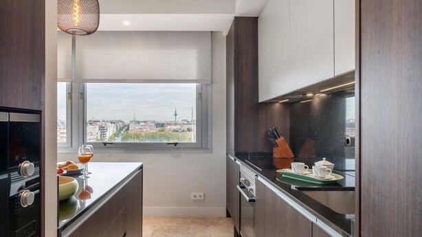 Eine moderne Küche mit dunklen Holzausführungen, einem großen Fenster mit Blick auf die Stadt, einem eingebauten Backofen und einer Arbeitsplatte mit einem Glas Orangensaft.