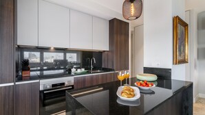 Eine moderne Küche mit dunklen Holzschränken, einer schwarzen Arbeitsplatte und einem eingebauten Ofen. Auf der Arbeitsplatte steht eine Obstschale mit Erdbeeren und ein Teller mit Croissants.