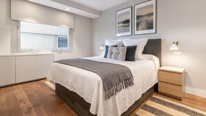 Ein modernes Schlafzimmer mit einem großen Bett, Nachttischen, einem Fenster und Kunstwerken an der Wand.