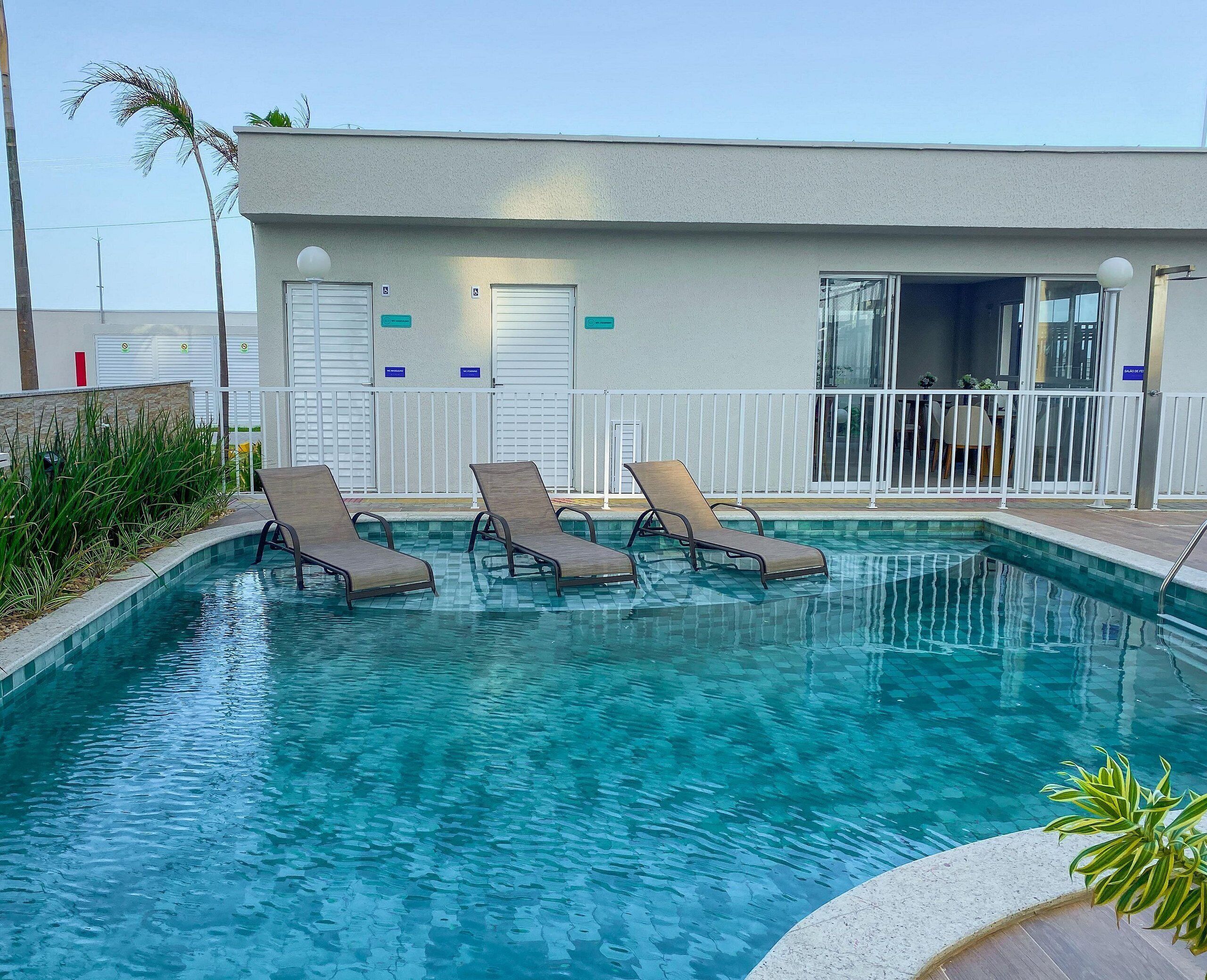 A swimming pool with lounge chairs, a building with a white exterior, and a palm tree.
