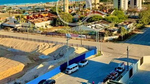 Un ensemble immobilier composé d’immeubles de grande hauteur, avec plusieurs tours, une plage en arrière-plan et un chantier de construction où l’on aperçoit des véhicules et une personne.