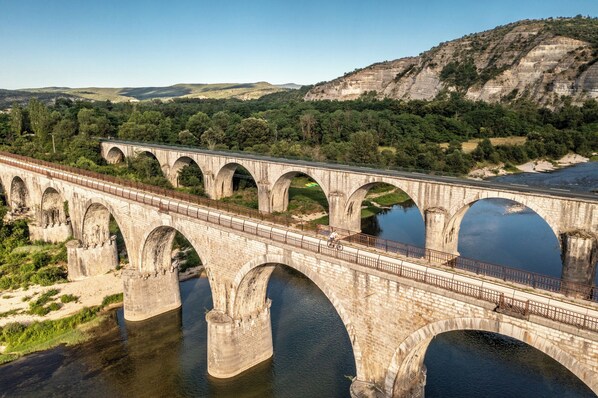 A large stone bridge with multiple arches spanning a river, surrounded by greenery and hills.