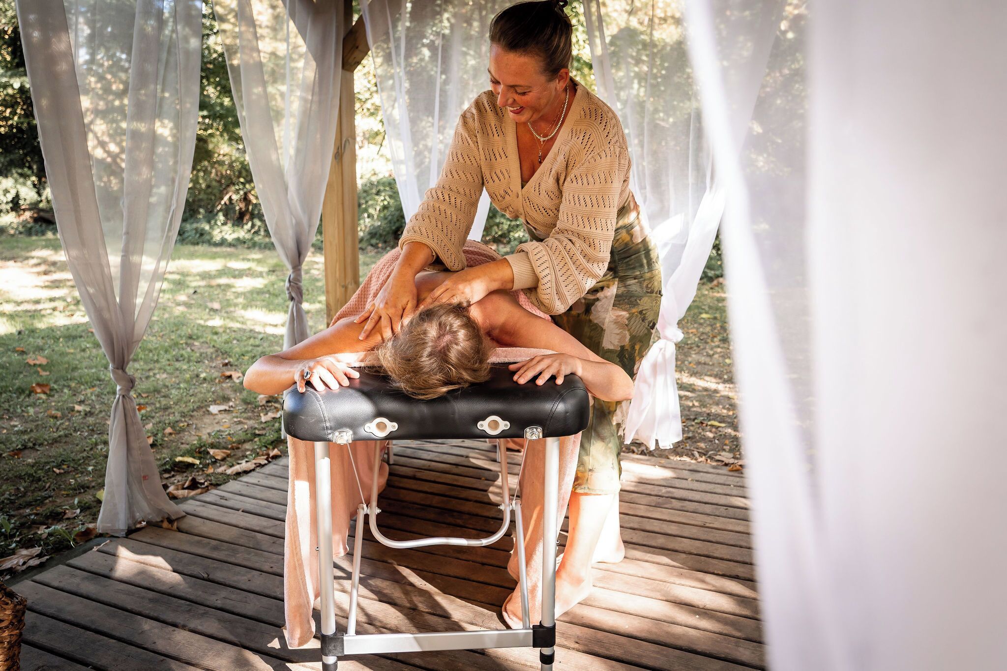 A massage table in an outdoor setting with a wooden deck and white curtains.