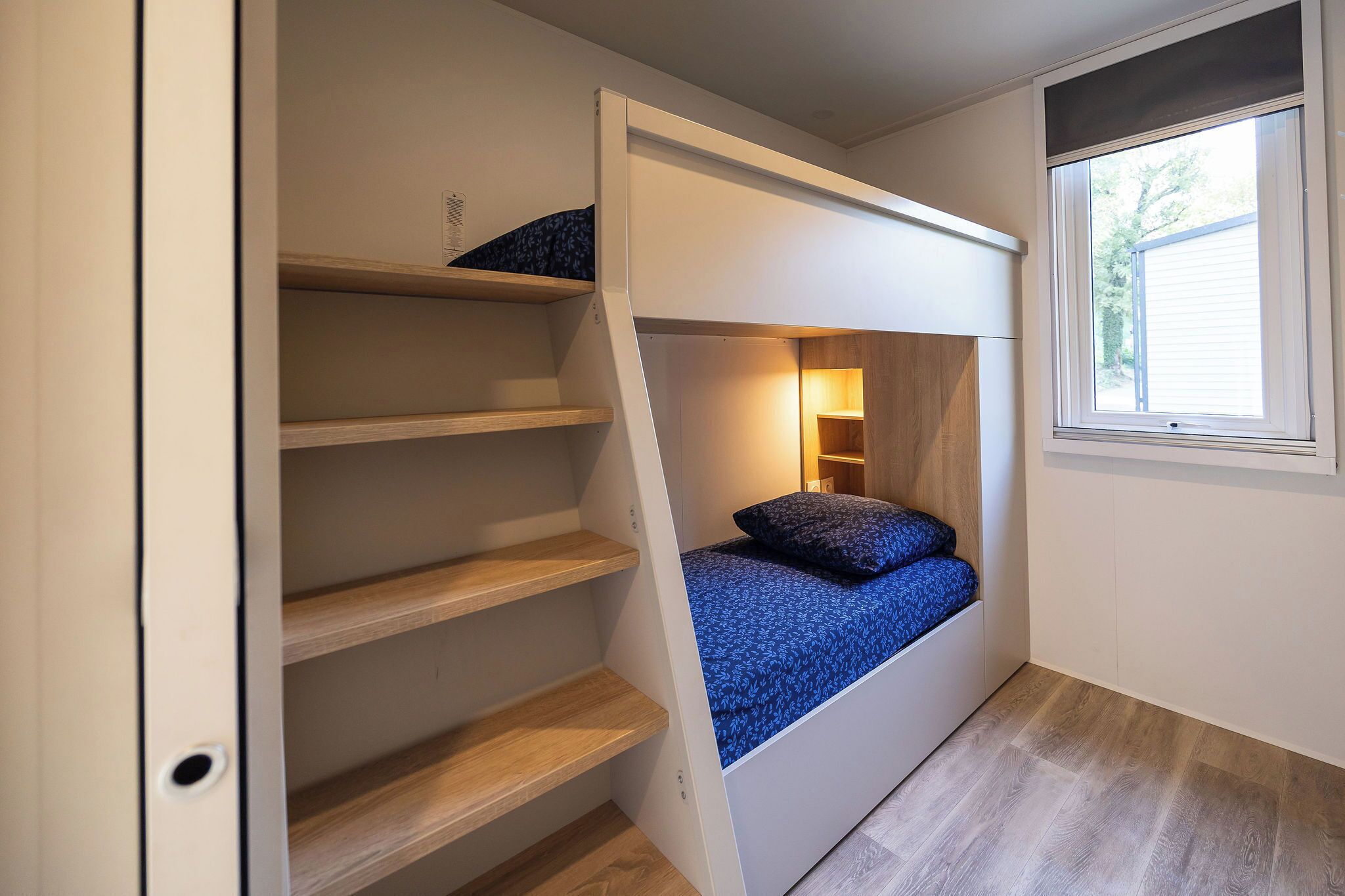 A compact room with a bunk bed, built-in shelving, and a window.