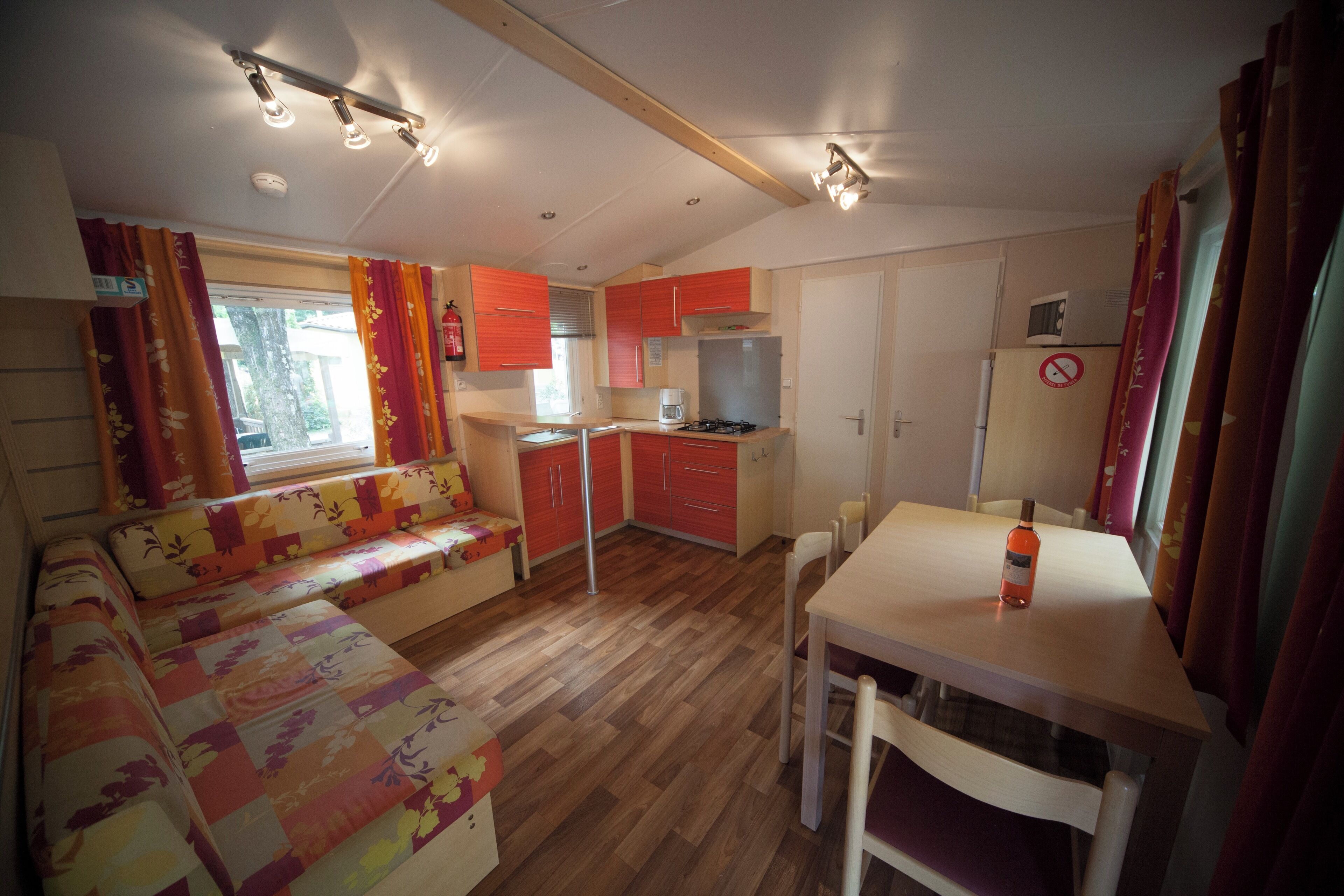 A compact kitchen with a dining area, a sofa, and a table with a bottle.