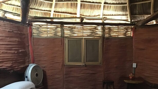 Una habitación con cama, ventana, ventilador y una mesita.
