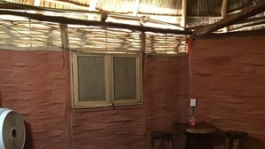Una habitación con cama, ventana, ventilador y dos taburetes.