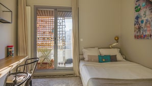 A bedroom with a bed, a desk, a chair, a lamp, and a view through a door. - Paris Center Latin residence (Paris)