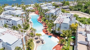An aerial view of a resort with a winding pool, palm trees, and beachfront properties. - Bakour Punta Cana Suites (Punta Cana)